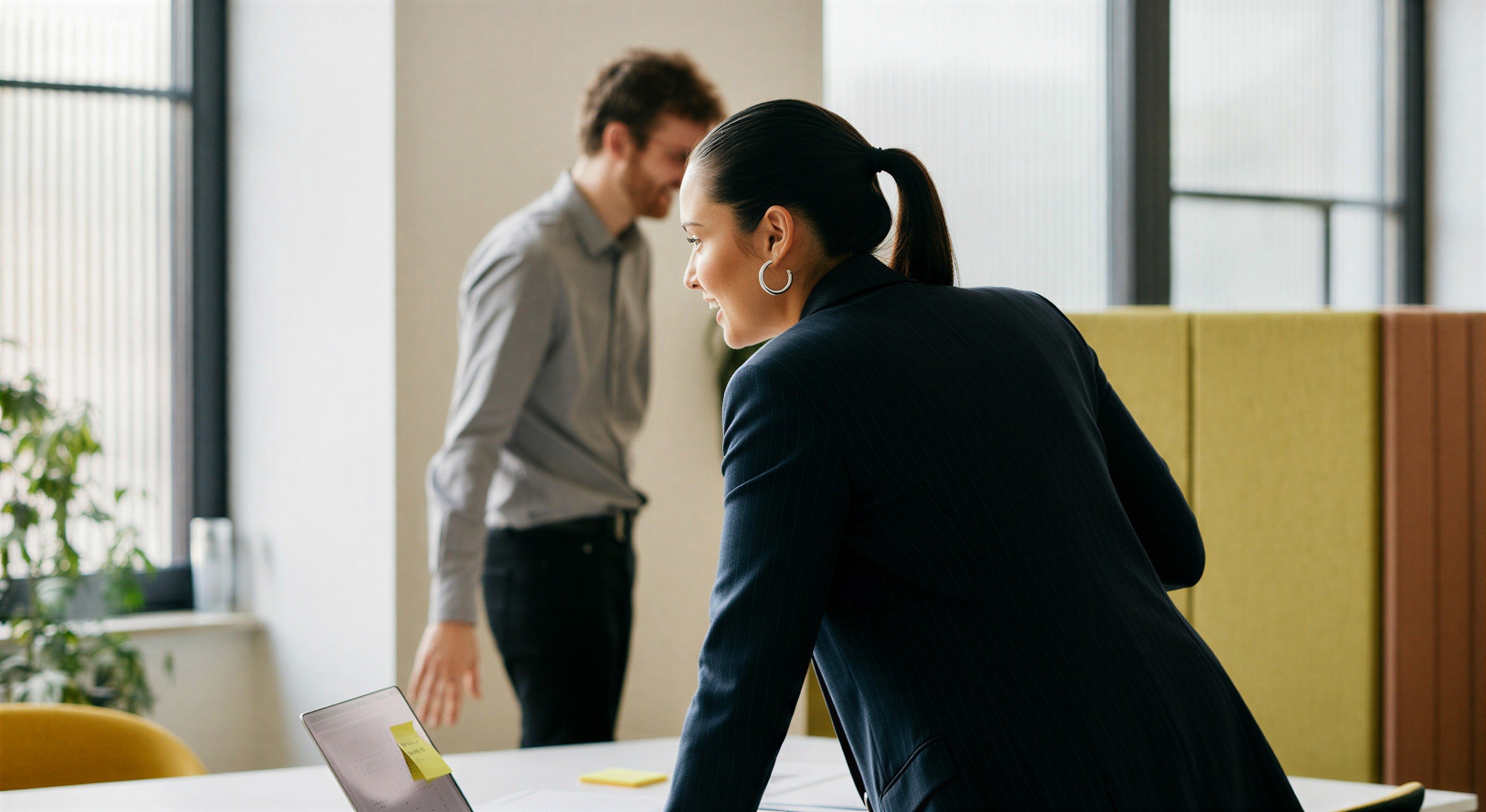 A woman leaning over a desk while a colleague stands behind her in a bright office.