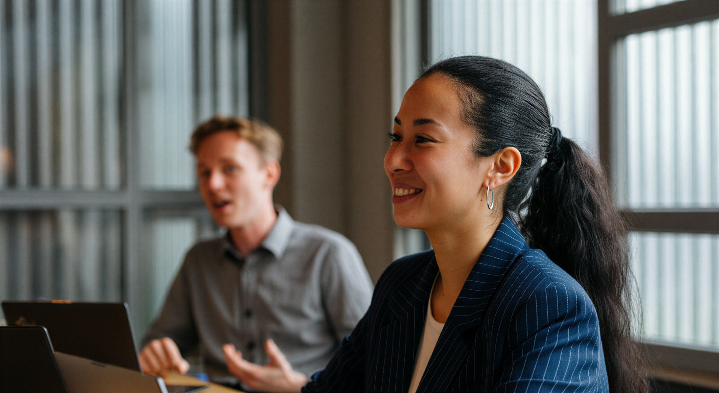 Two colleagues talking across a table in a bright office.